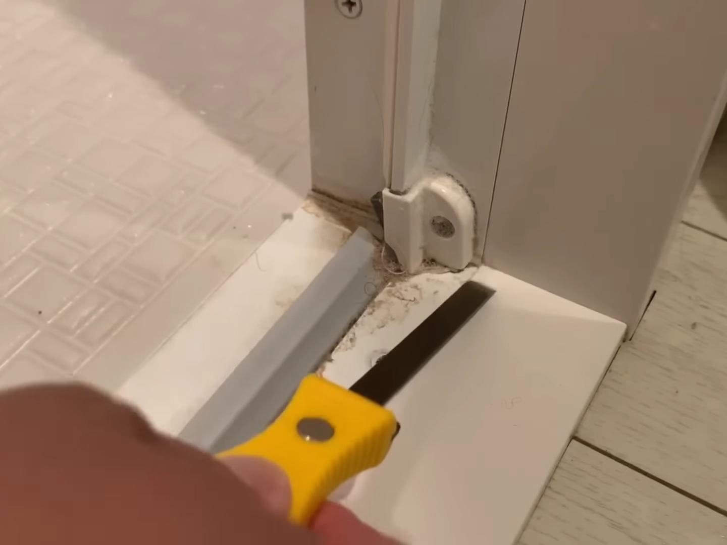 皮すきで浴室ドアの下を掃除する男性