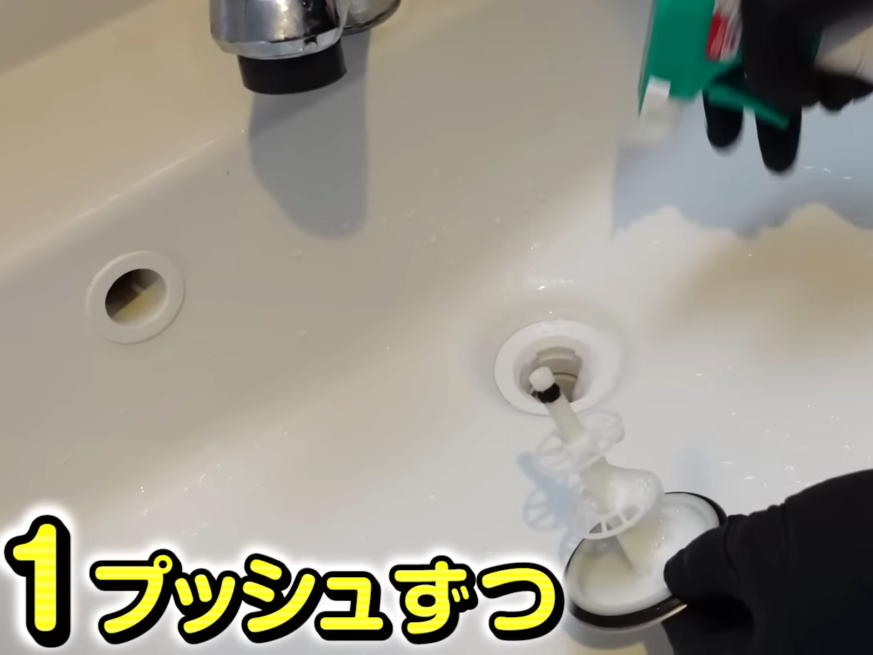 洗面所の排水口にキッチン泡ハイターを吹きつける男性