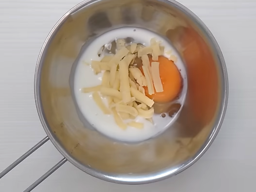 ボウルに入れた卵、牛乳、チーズ、塩を混ぜ合わせる女性