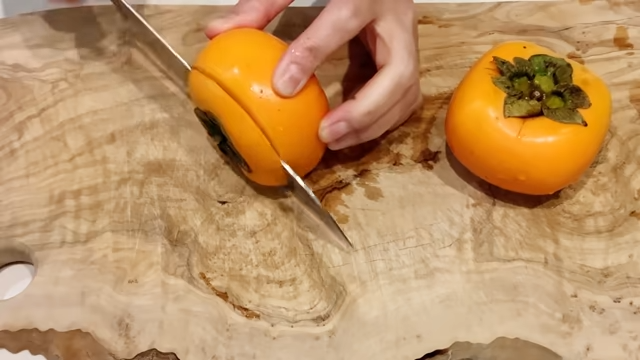柿のヘタを包丁で切り落とす女性