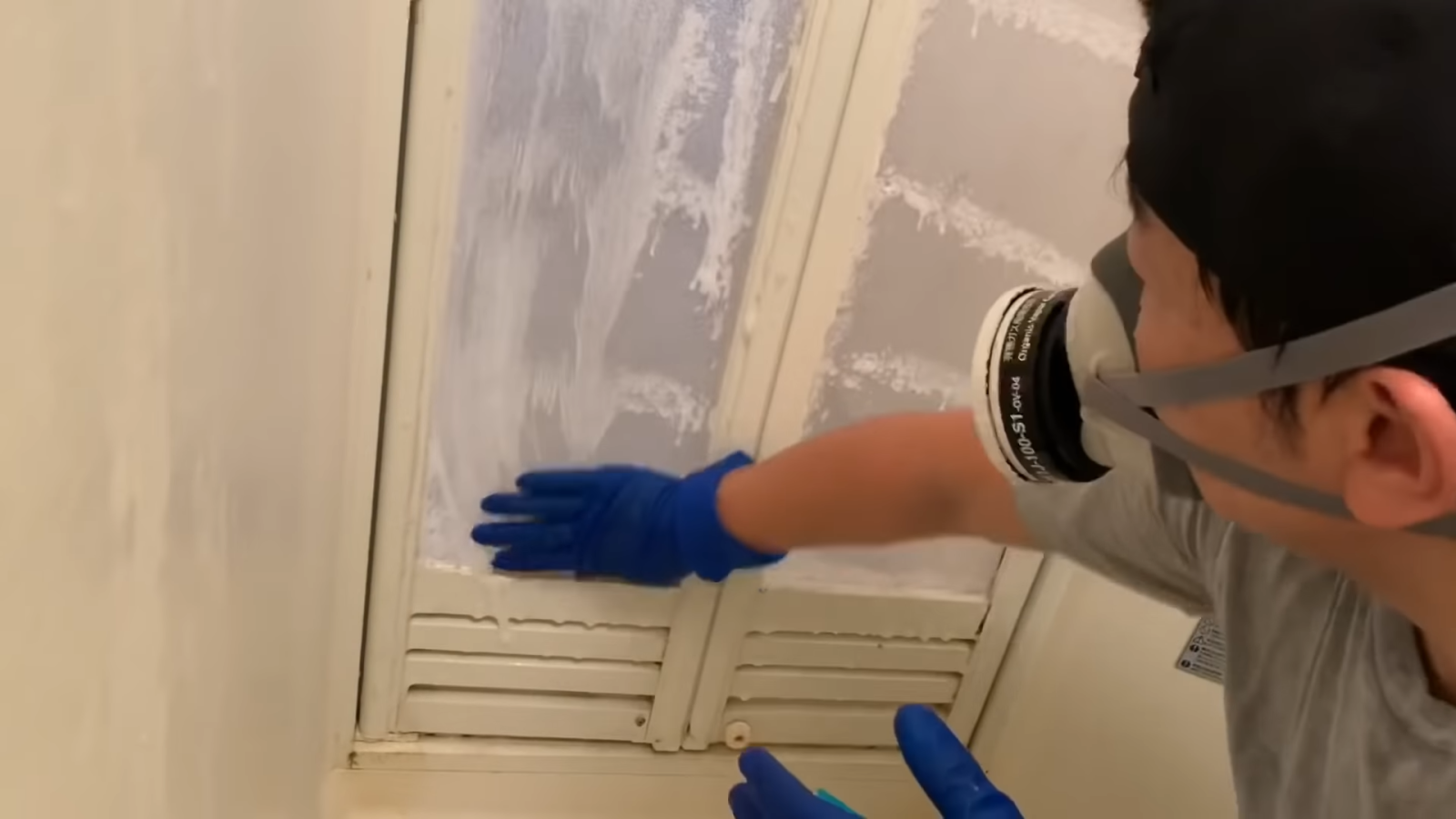 お風呂場の扉につけた洗剤をゴム手袋で伸ばす男性