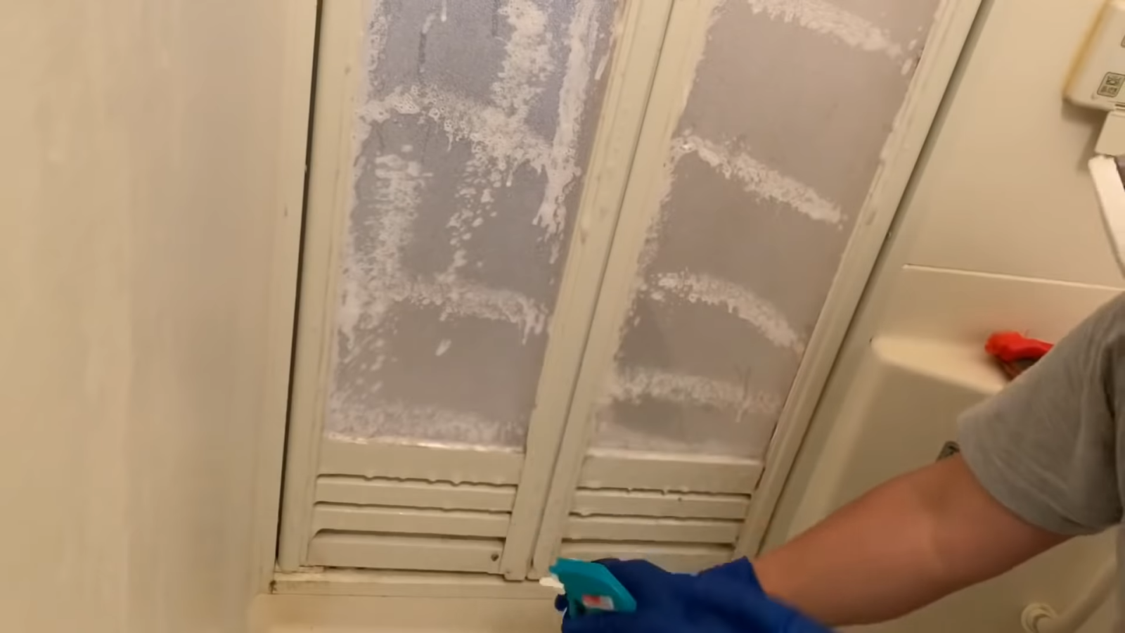 お風呂場の扉に塩素系洗剤を吹きかける男性