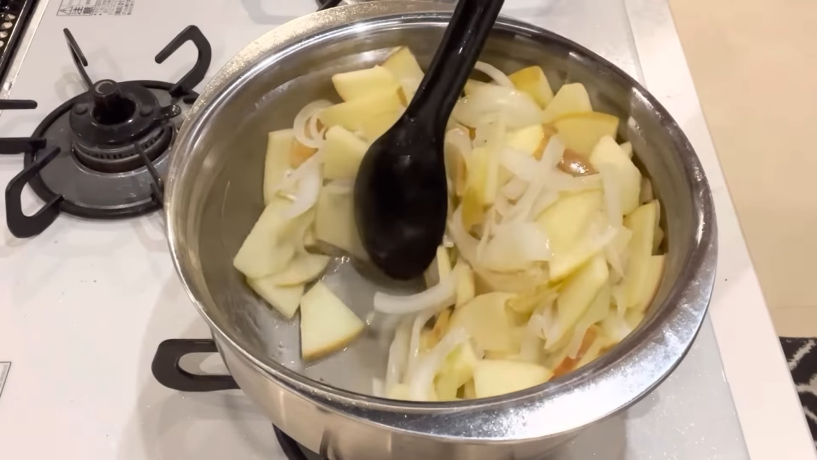 玉ねぎとりんごを鍋で炒める女性