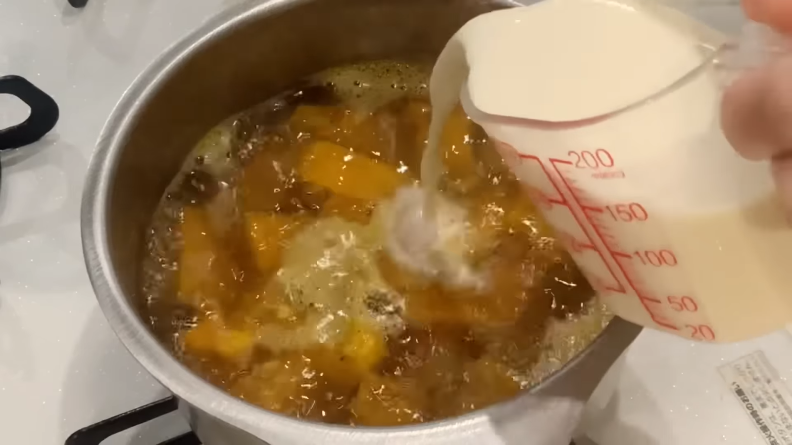 かぼちゃが煮えた鍋に豆乳を入れる人