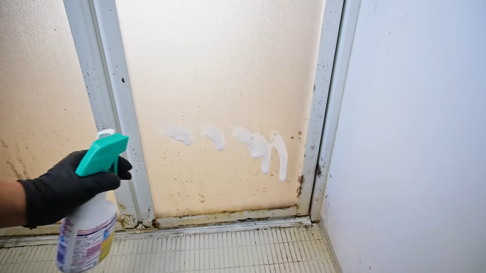 カビ汚れがついたお風呂場のドアに洗剤をまく男性