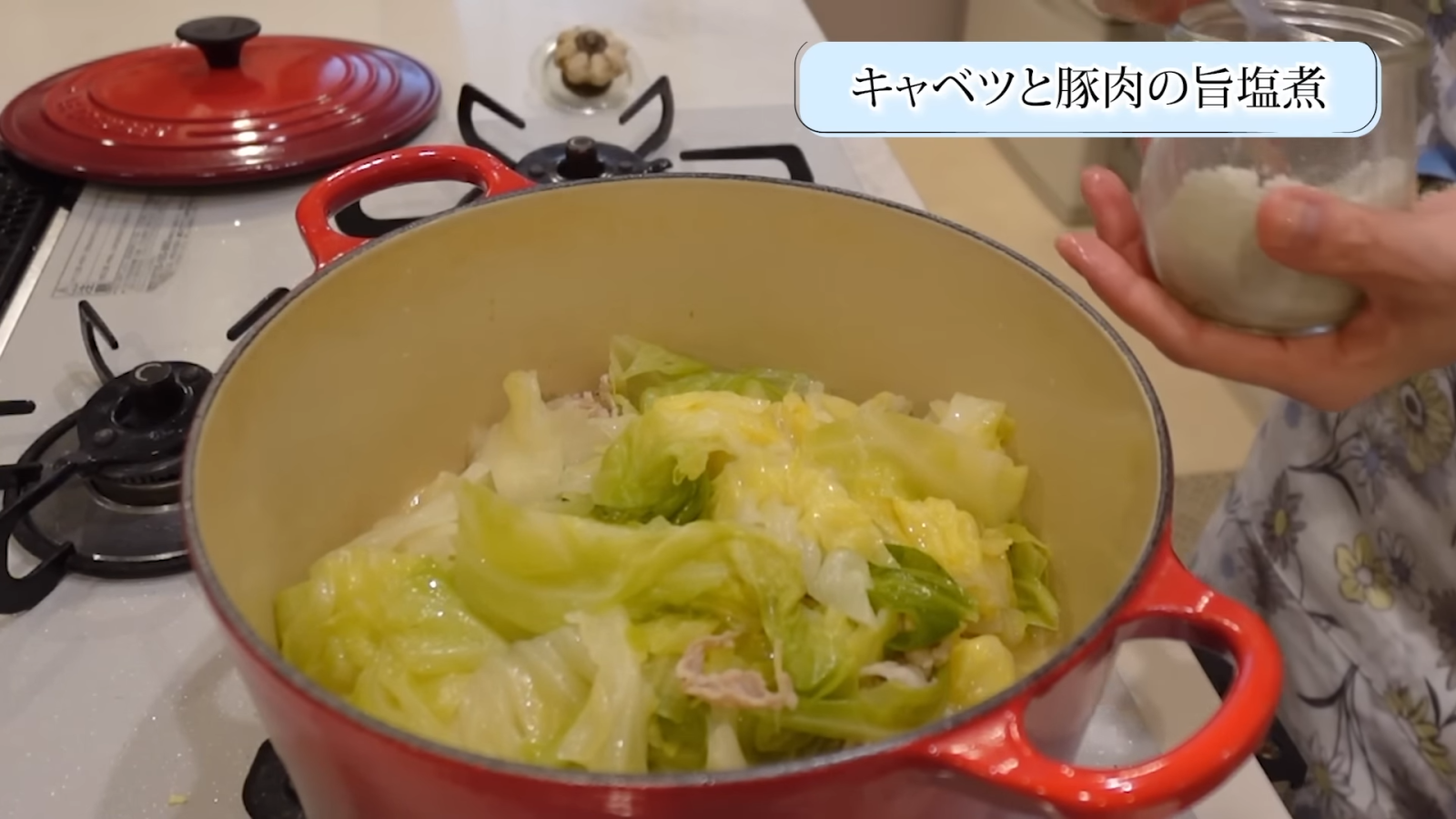 鍋にあるキャベツと豚肉を菜箸で混ぜ合わせる女性