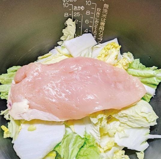 炊飯器に鶏むね肉、白菜、調味料を入れる男性