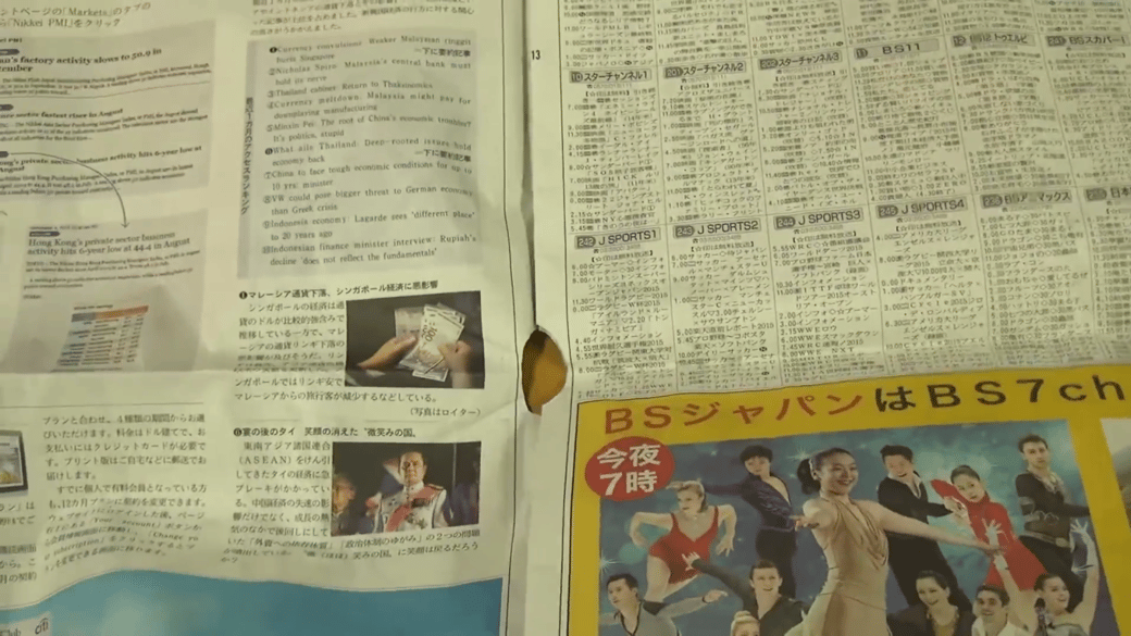 新聞紙にハサミで丸い穴を開けた男性