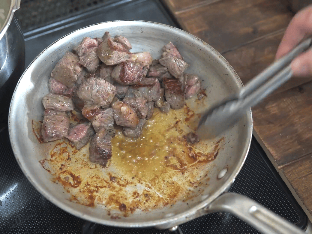 フライパンで肉を焼く男性