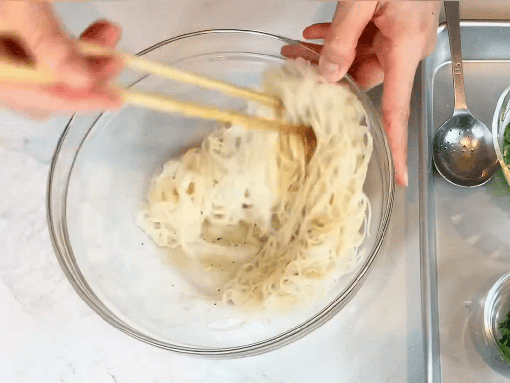 そうめんをボウルに入れた調味料と混ぜ合わせる女性