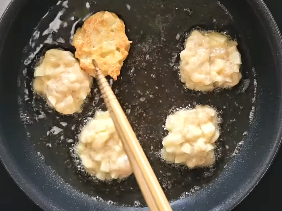 フライパンでで揚げ焼きをしているナゲットを菜箸で裏返す女性