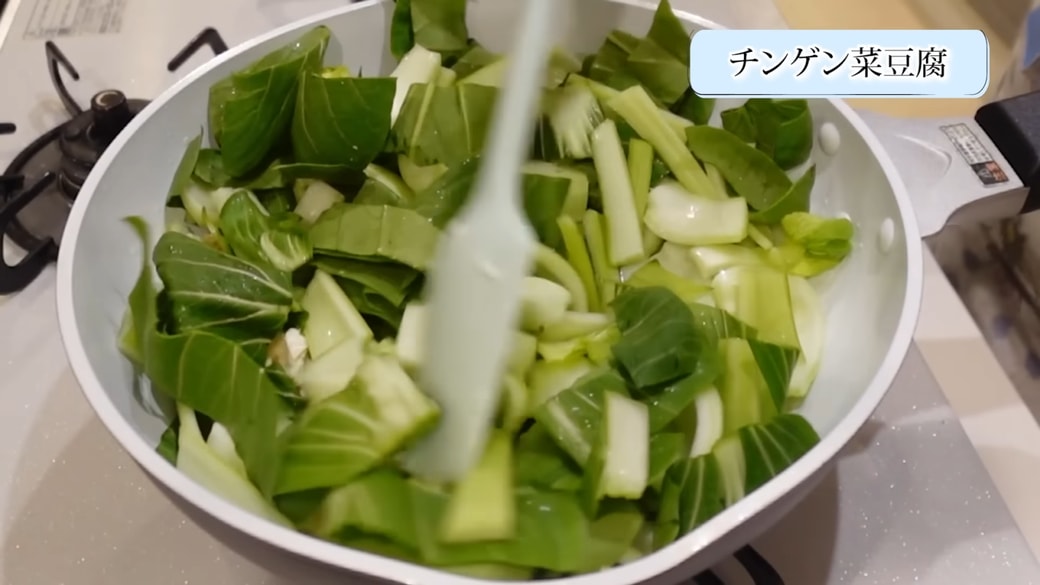 フライパンでチンゲン菜と焼き豆腐を炒める女性