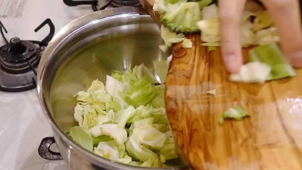 鍋に野菜を入れる女性