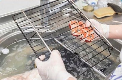 魚焼きグリルの網を掃除する人