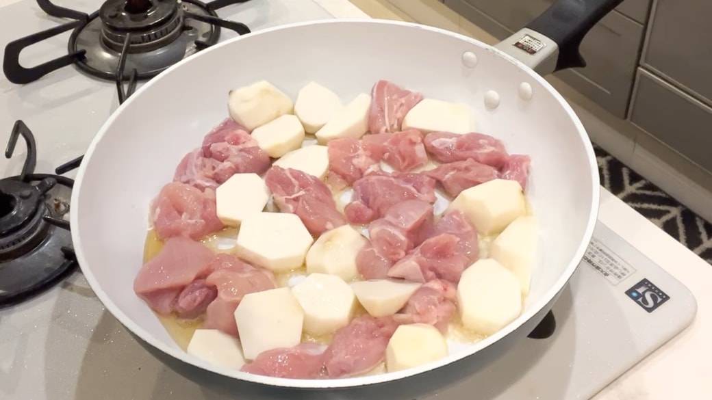 フライパンで里芋と鶏もも肉を炒める女性