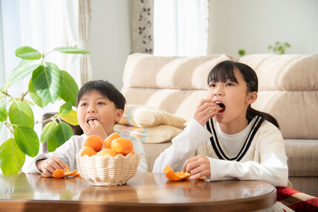 こたつでみかんを食べている子ども