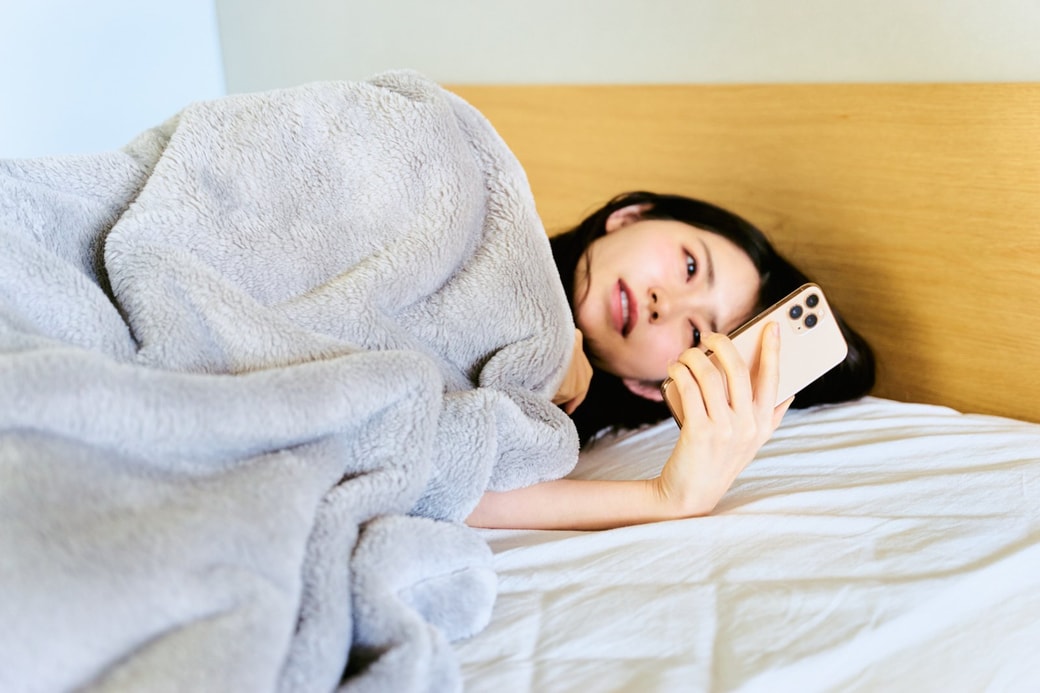 ベッドでスマホをチェックする女性