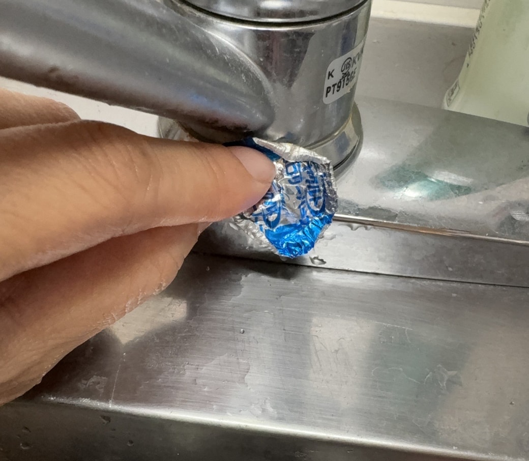 蛇口の付近をヤクルトの蓋を使って掃除する手