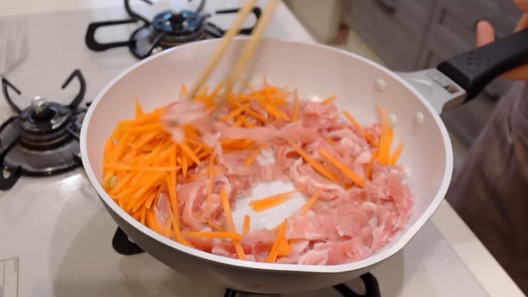 フライパンで豚肉とニンジンを炒める人