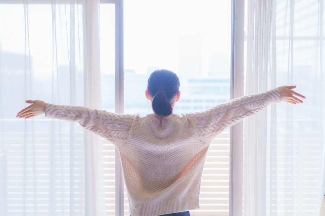 窓を開けて深呼吸する女性