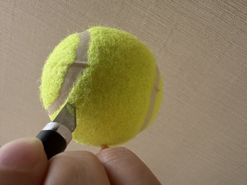 テニスボールに口になる切りこみを入れる様子
