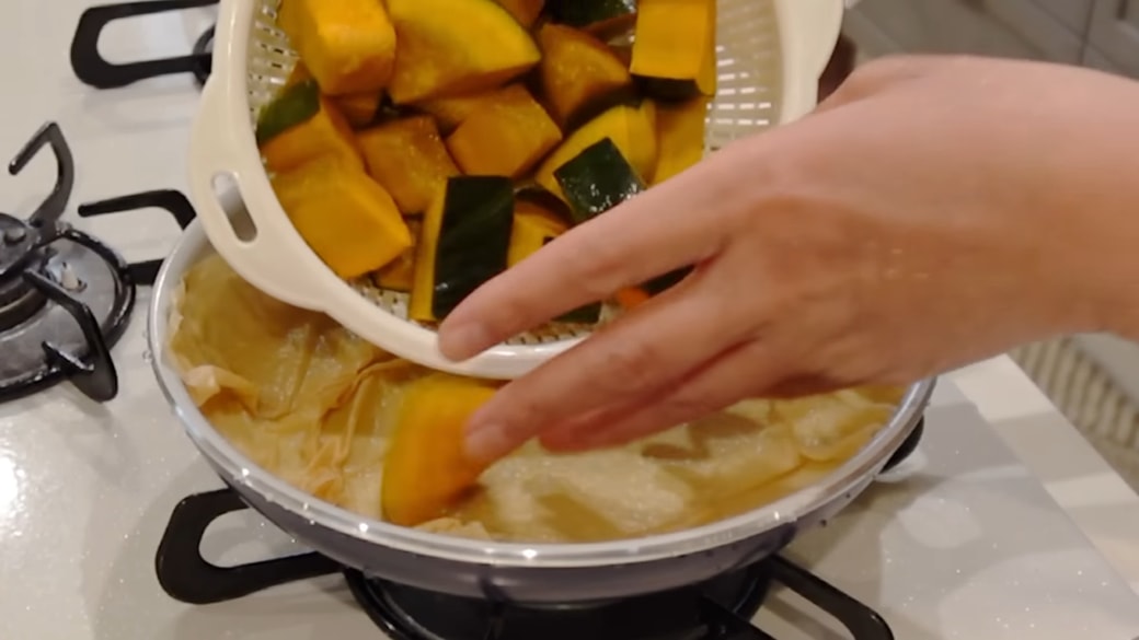 キッチンペーパーをしいたフライパンにかぼちゃを並べる人