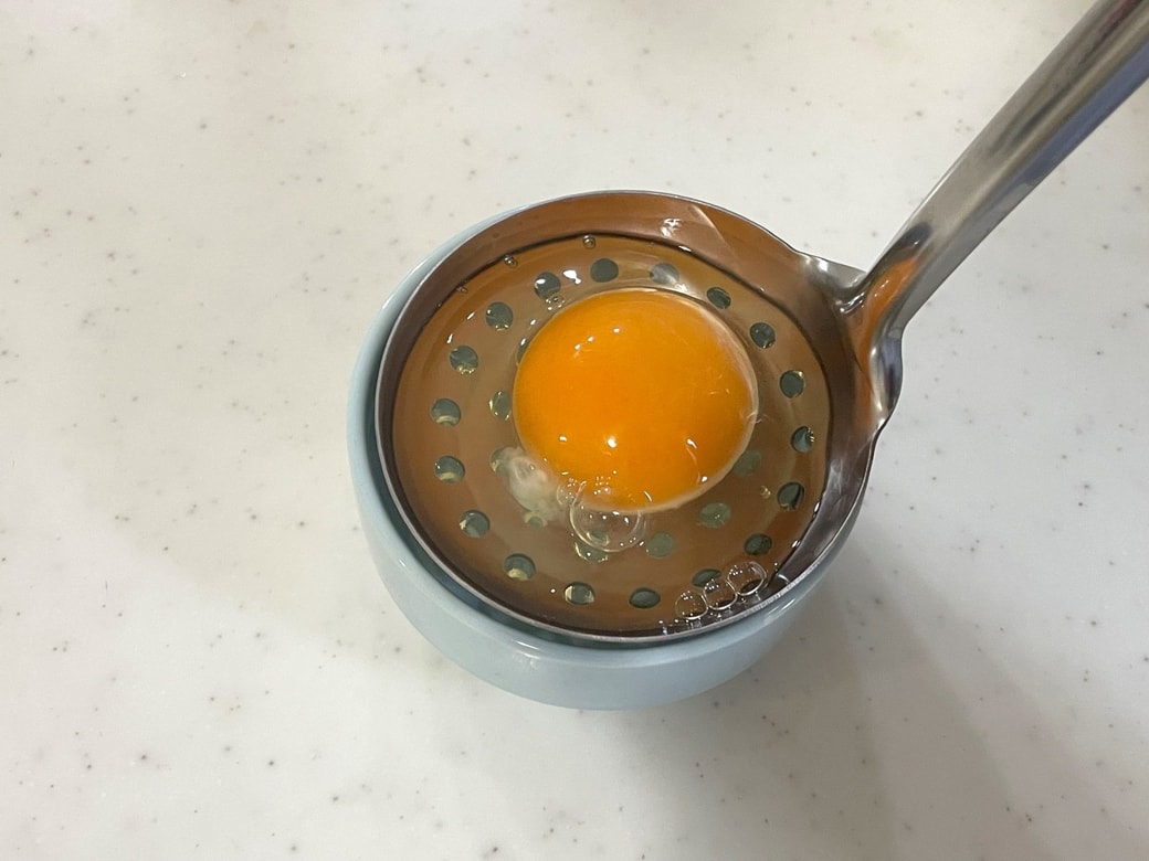 お玉に卵を割り入れる