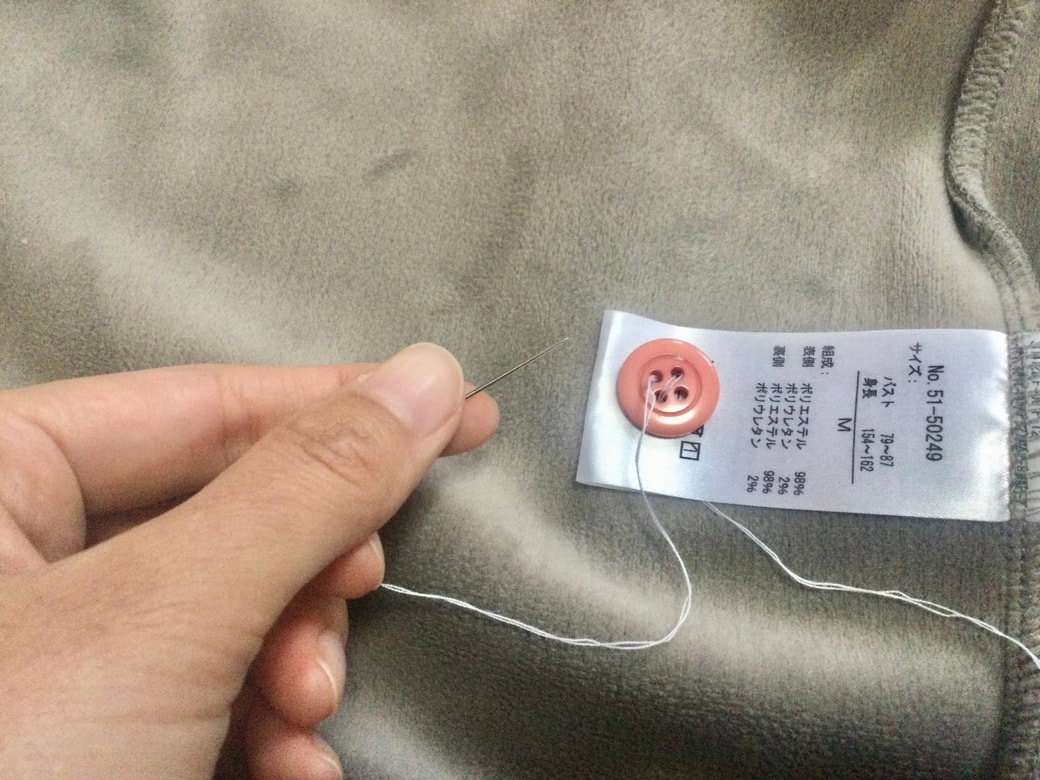 服の洗濯タグにボタンを縫い付ける