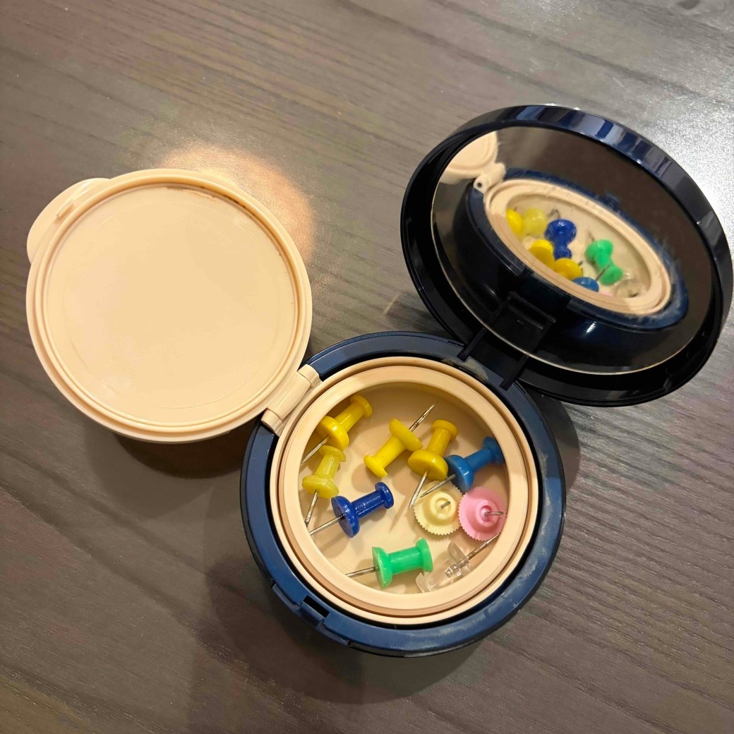 ファンデーションの空き容器に画びょうをいれているところ