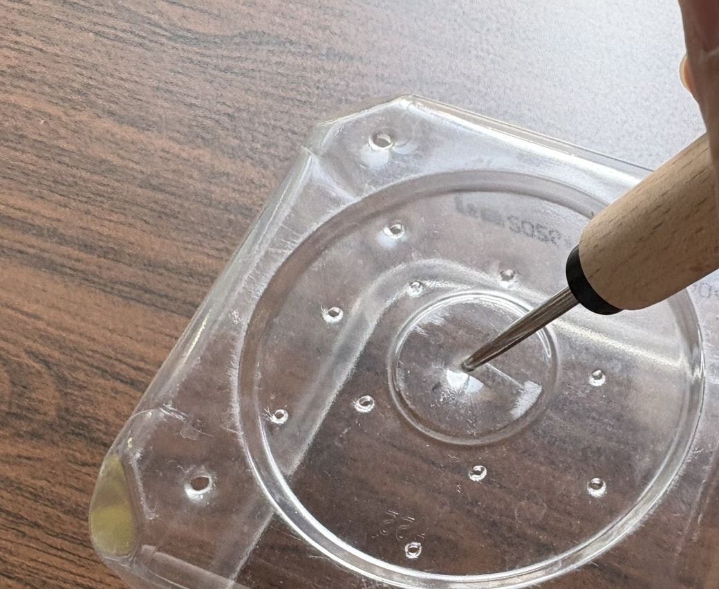 お味噌の空き容器に目打ちで穴をあける様子