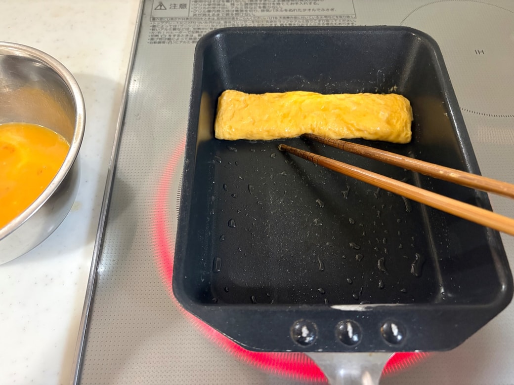 卵焼き器で半量の卵液を焼いて巻く