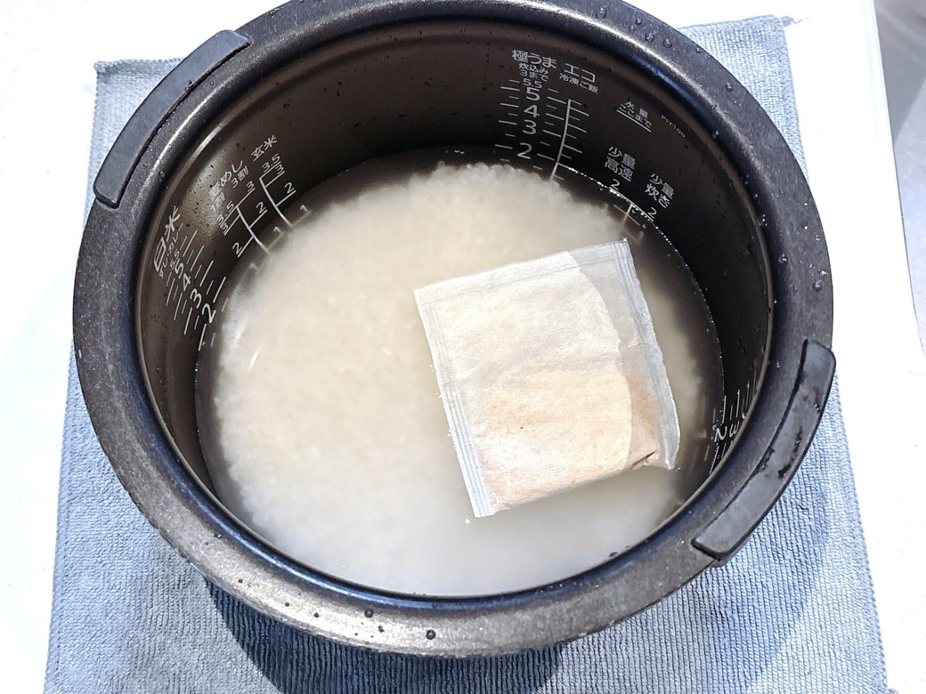 洗ったお米に水を注ぎ、だしパックを入れる