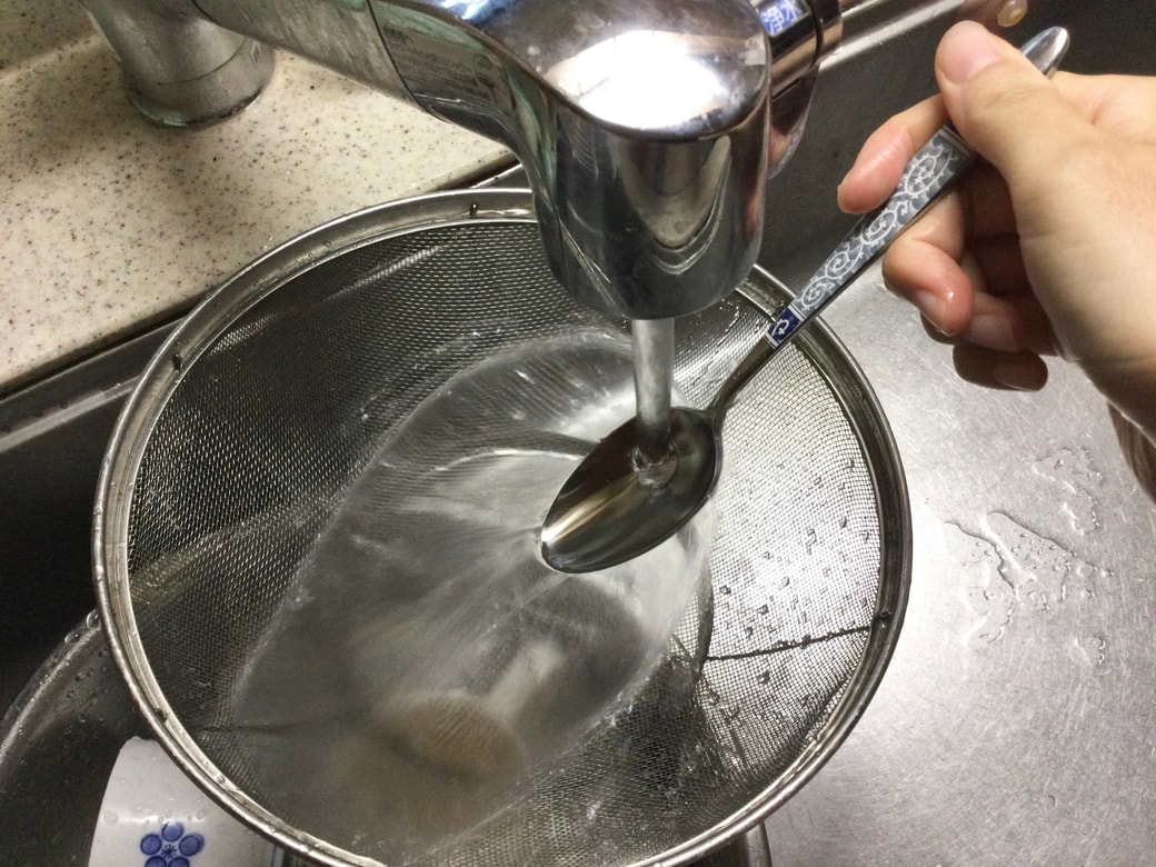 スプーンの面に水をあててザルを洗う