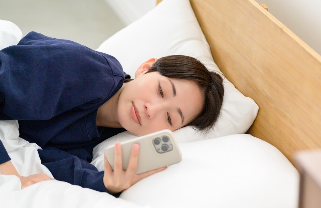ベッドでスマホを見る女性