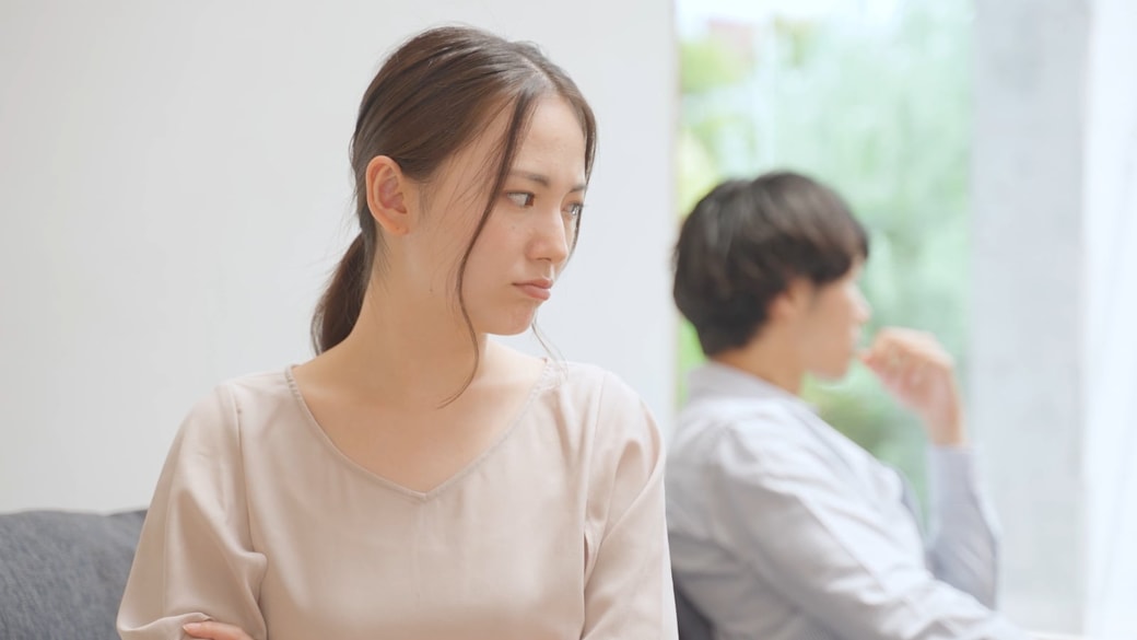 苛立つ女性と背を向け合う夫婦