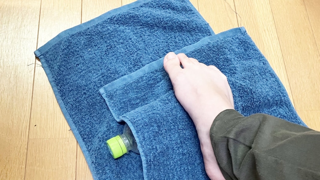 タオルで包んだ凍らせたペットボトルを足裏で転がしている様子