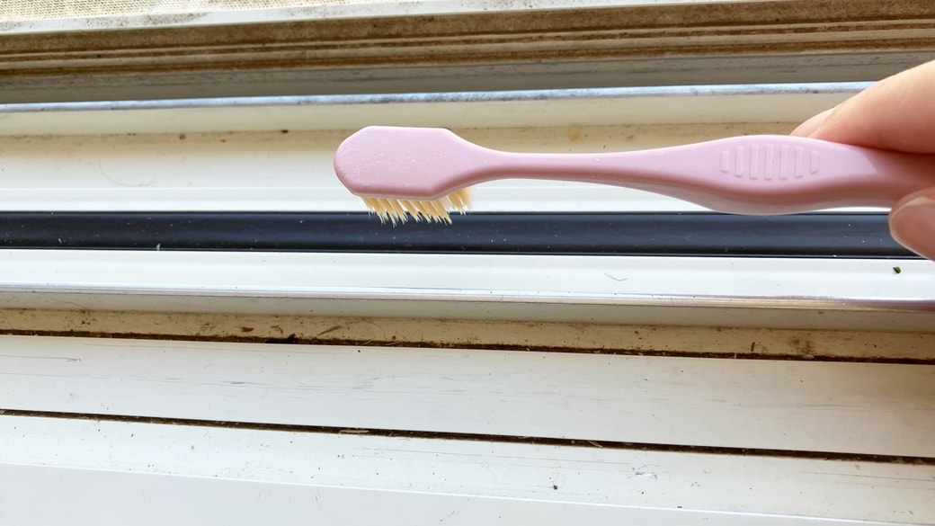 歯ブラシで窓サッシの掃除をしている様子