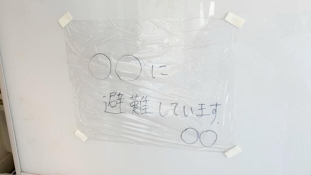 「〇〇に避難しています」と書いたラップを貼りつけている様子