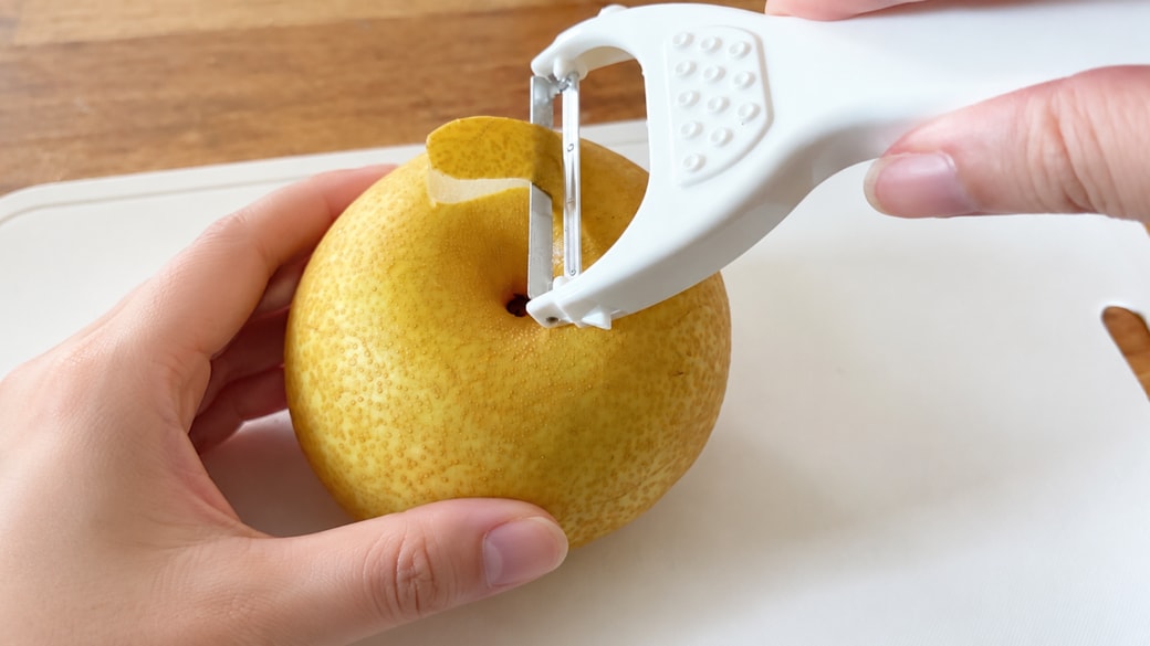 梨の丸みにそってピーラーで皮をむいていく様子
