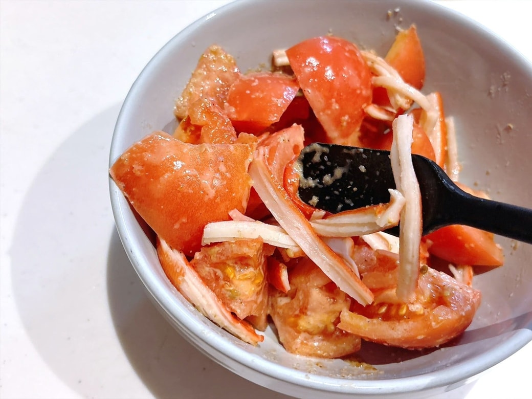 手順2.トマトを食べやすい大きさにカットし、かにかまをほぐしたら、合わせ調味料が入っている器に入れて混ぜる